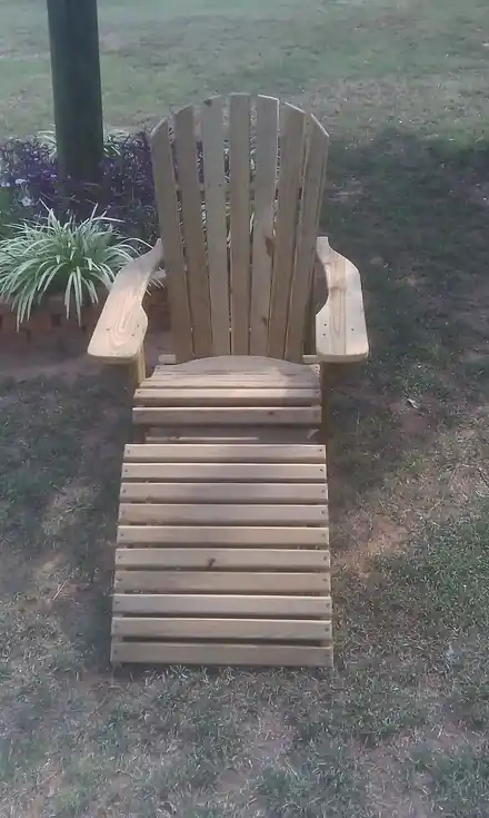 An Adirondack chair with a footrest standing on the grass
