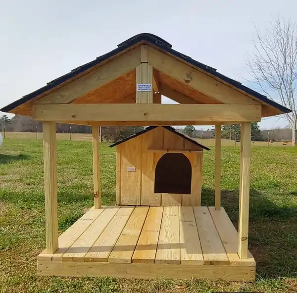 A dog house sitting on a decked pavilion with a gabled roof