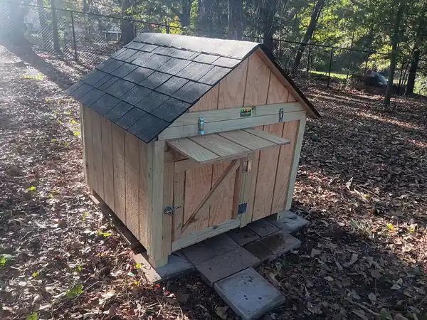 A shingled house with a latched awning door sitting in leaf litter