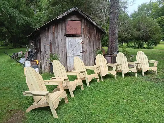 Five light-wood Adirondack chairs in front of a weathered barn