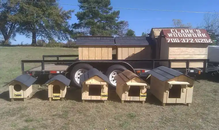 A trailer painted with the Clark's Woodwork name and phone number, with a row of pet houses lined up in front