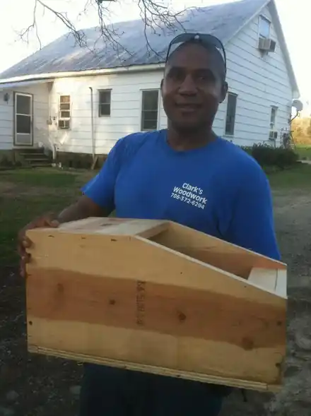 A man in a Clark's Woodwork shirt holding a nesting box